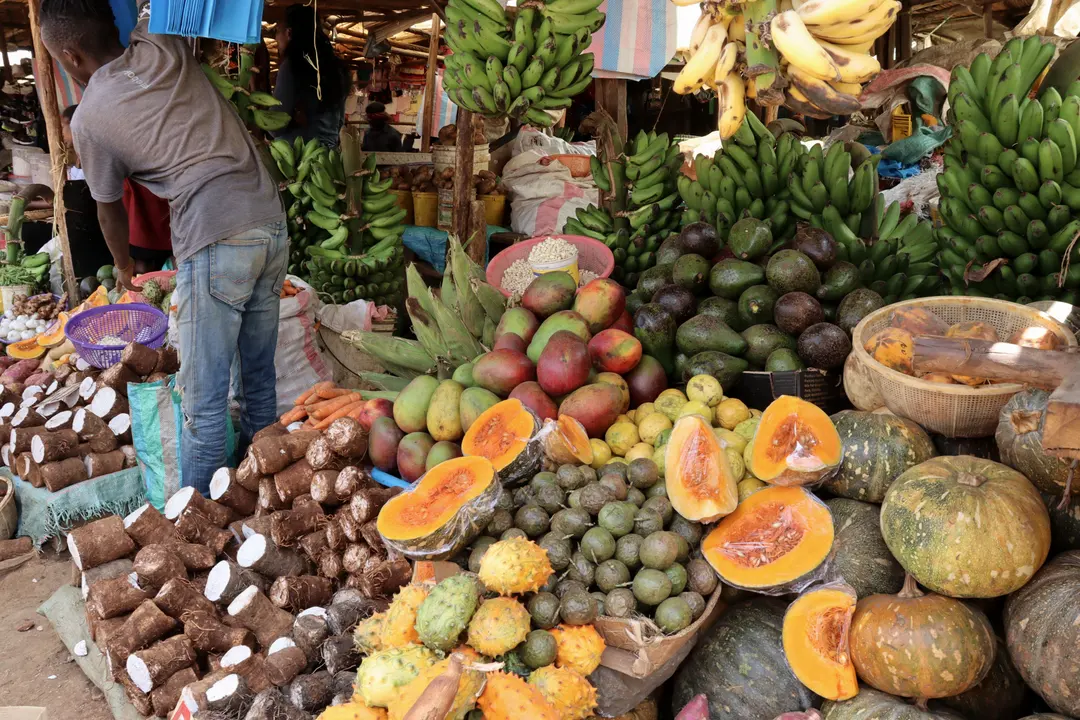 A Kenyan produce market stall stacked with bananas, mangoes, papaya and pumpkins.